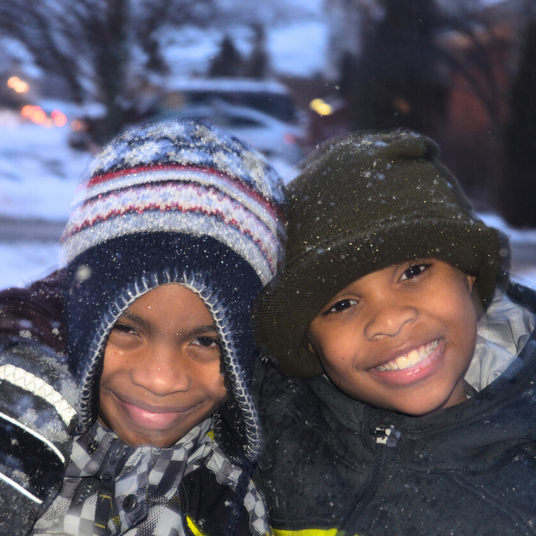 Two boys outside in the snow bundled up. Shop the Safe Haven store.